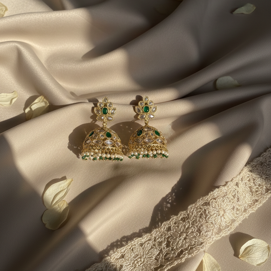 Gold and green earrings on a textured fabric surface with floral petals.