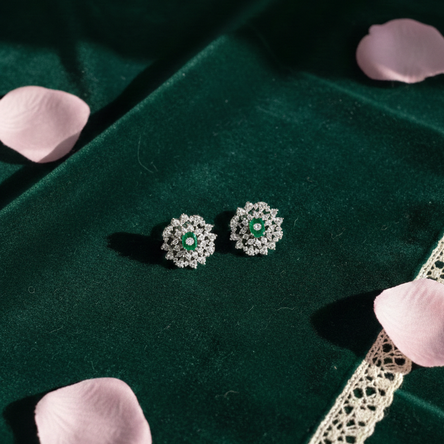Silver earrings with green gemstones on a green velvet surface with pink petals and lace.