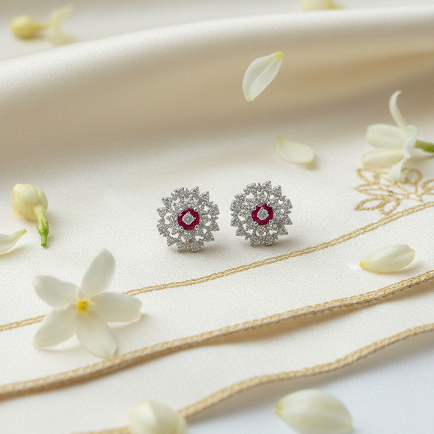Silver earrings with red gemstones on a white surface with flowers