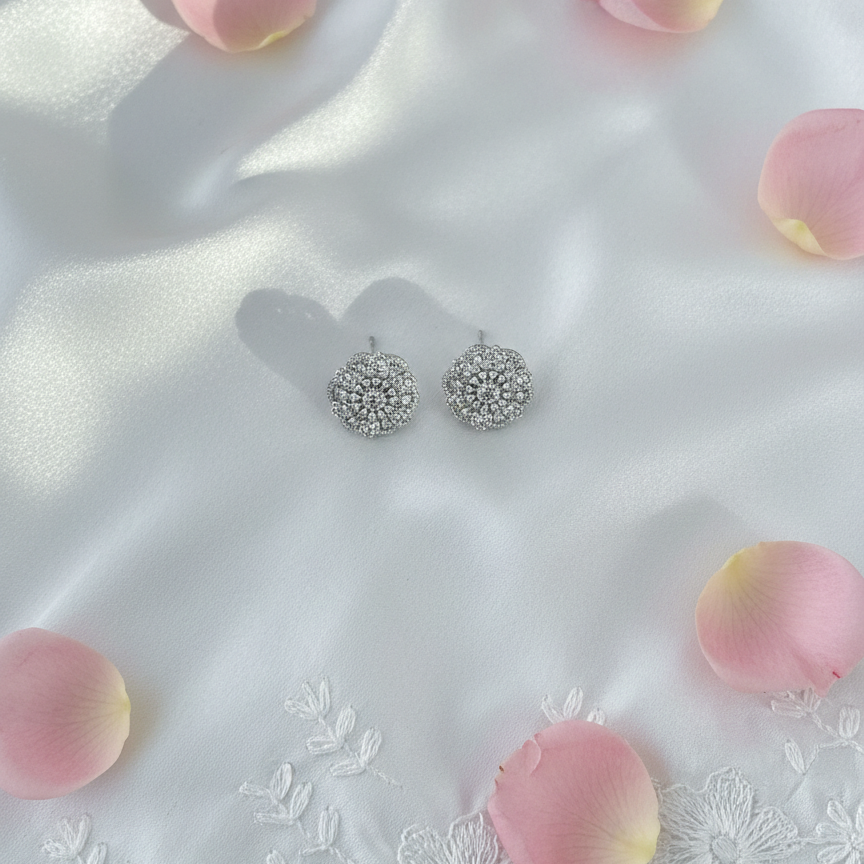 Silver earrings on a white fabric background with pink rose petals